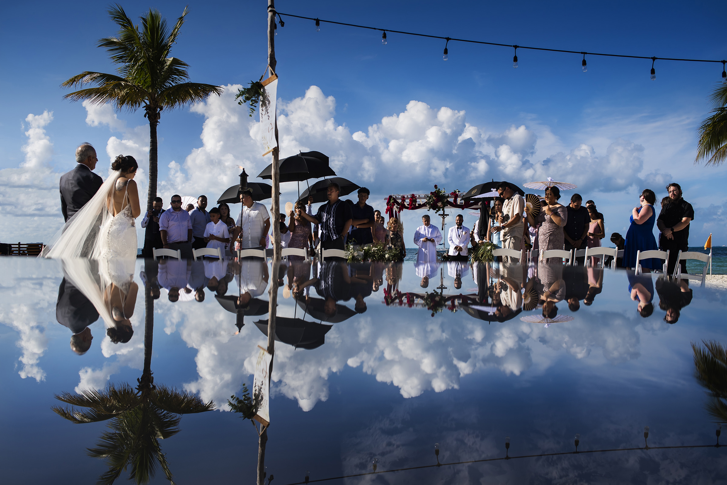 reflected-clouds-blue-skies-and-umbrellas-at-outdoor-ceremony-processional-photo-by-lax-photography