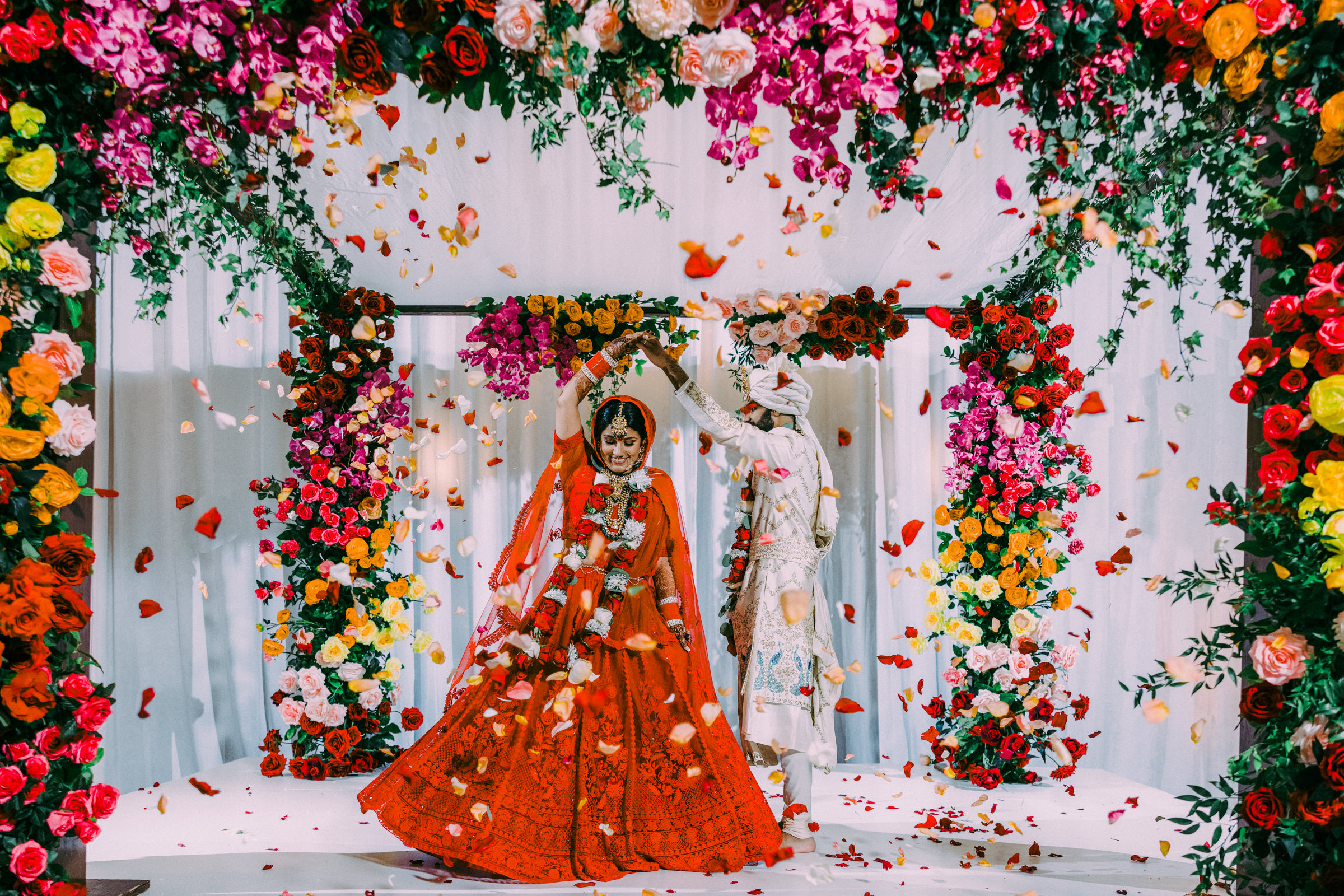 Indian couple under tent with colorful flowers and petals everywhere Nat Wongsaroj Photography