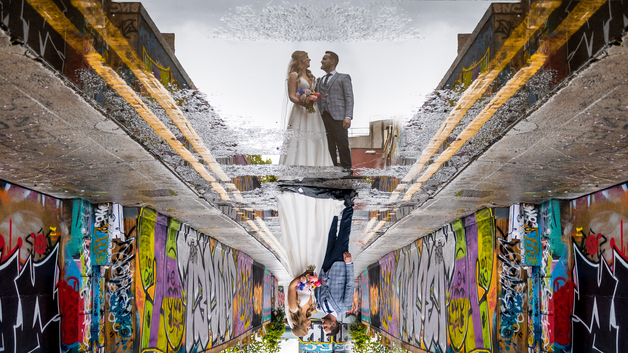 couple-pose-at-perspective-point-with-reflected-colorful-graffiti-wall-photo-by-john-gillooley