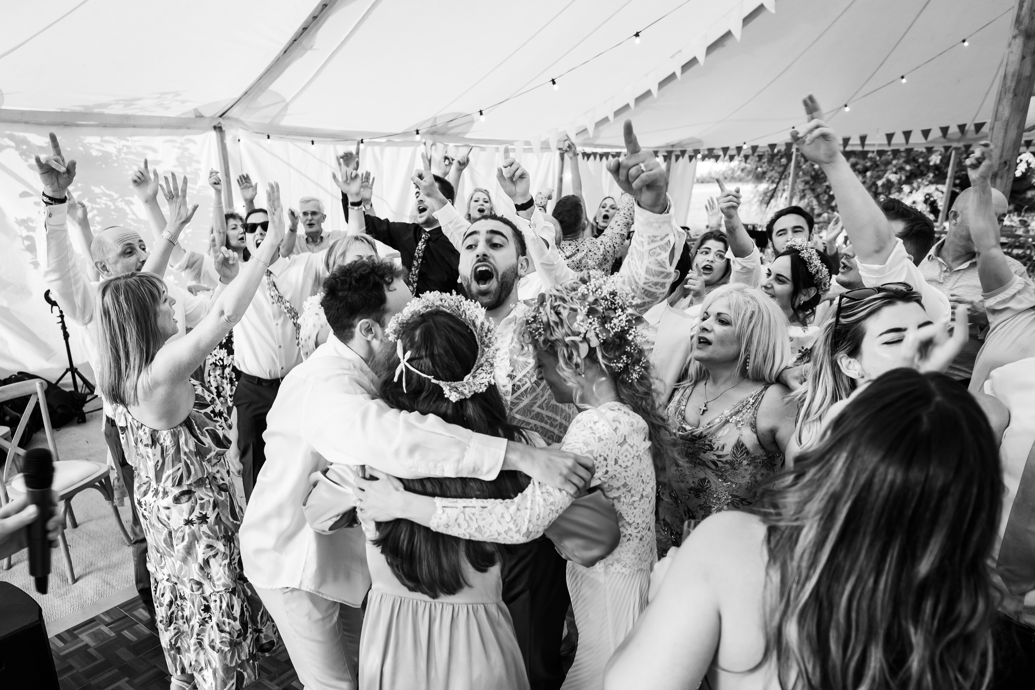 Friends gather around bride and groom and hug on dance floor