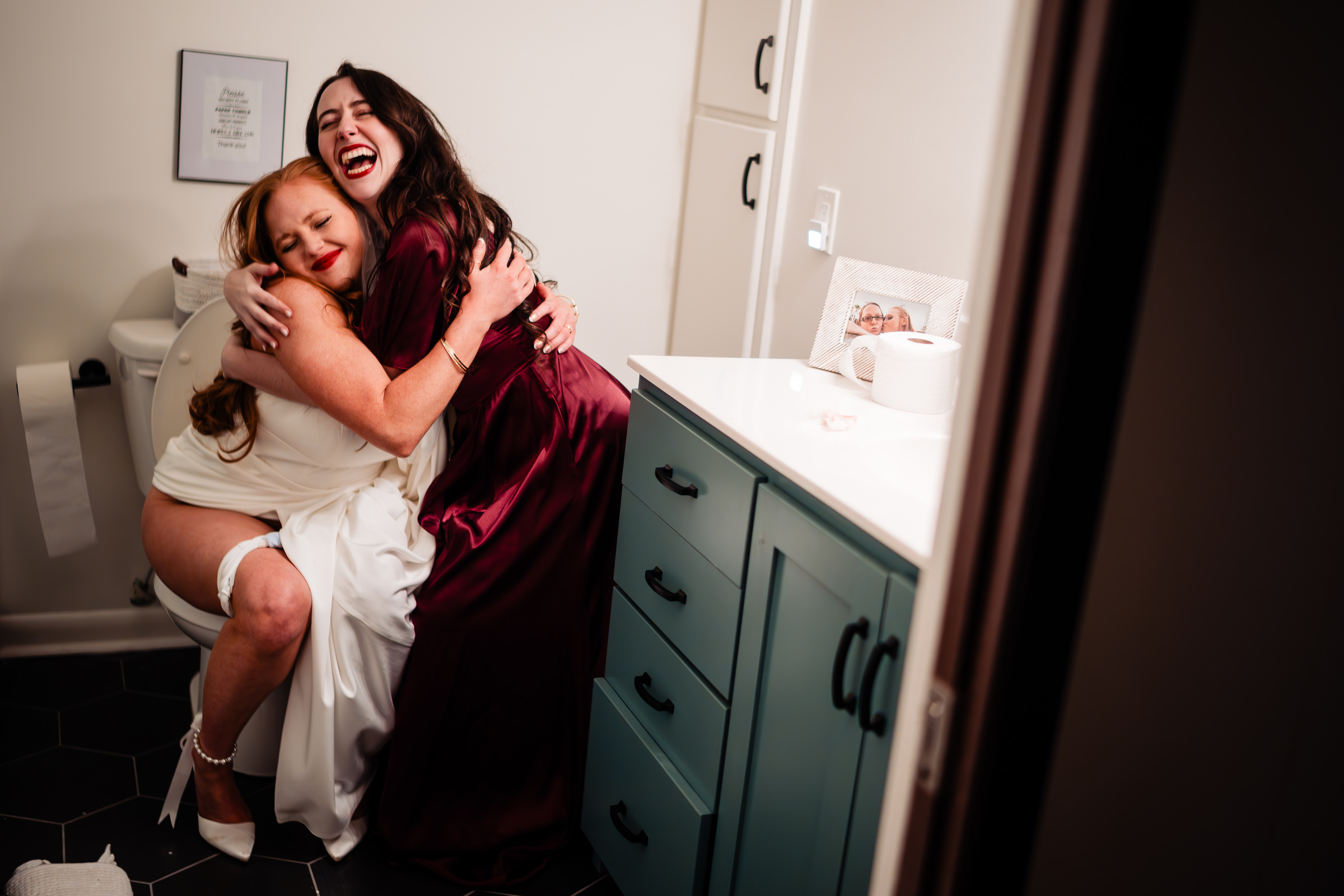 Bride on toilet hugs bridesmaid - photo by Vinson Images