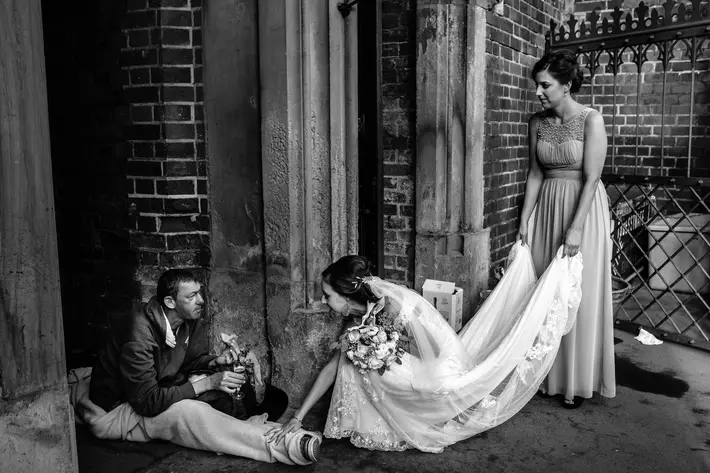 Black and white photo of compassionate bride and homeless man by Yves Schepers