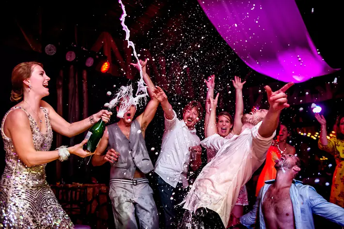 Bride pops champagne over partying guests - photo by Davina plus Daniel