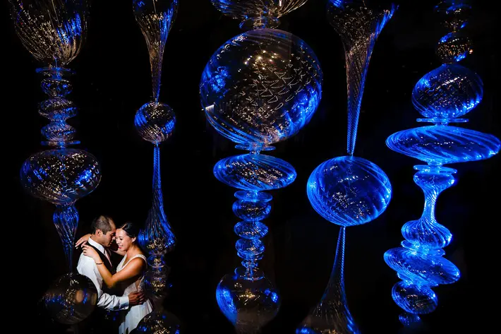 Couple portrait under blue lit glass sculptures by Jos & Tree