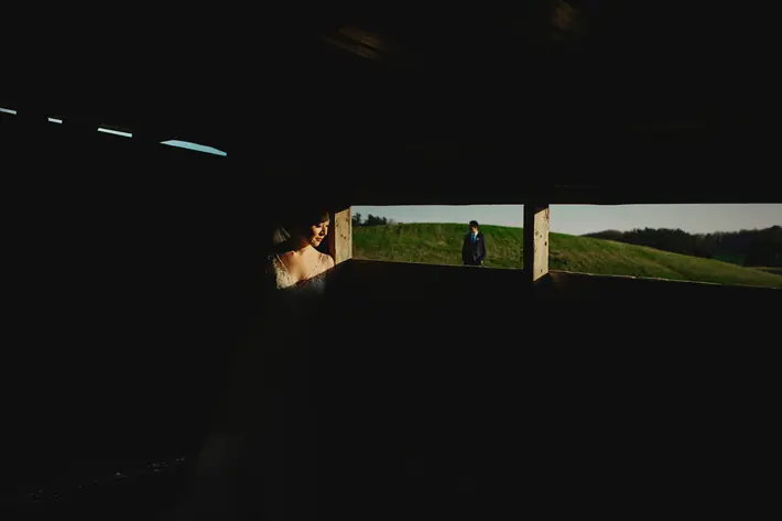 featured-bride-in-dramatic-afternoon-light-through-window-with-groom-in-field-in-background-worlds-best-wedding-photos-fer-juaristi