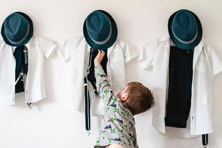 Little boy reaches for his wedding clothes and blue felt hat - photo by Andrew Billington - England