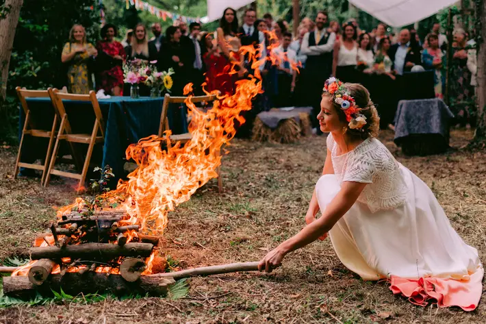 Bride wearing lace dress and floral crown stoking campfire - photo by Rich Howman - England
