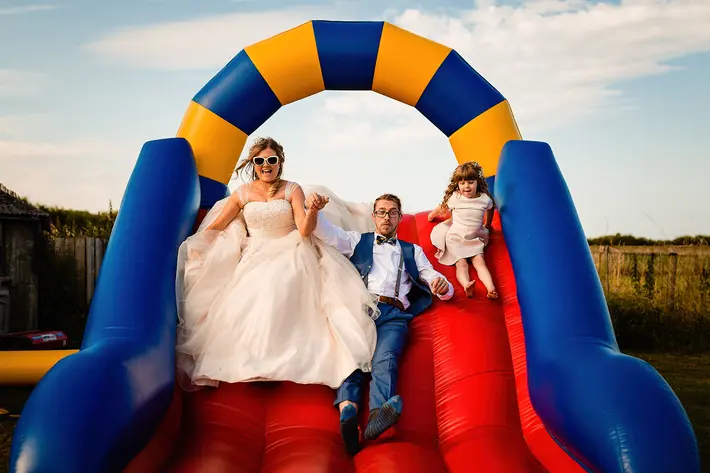 Bride, groom and little girl on blow-up slide, photo by Emma plus Rich, UK photographers wedding photographers