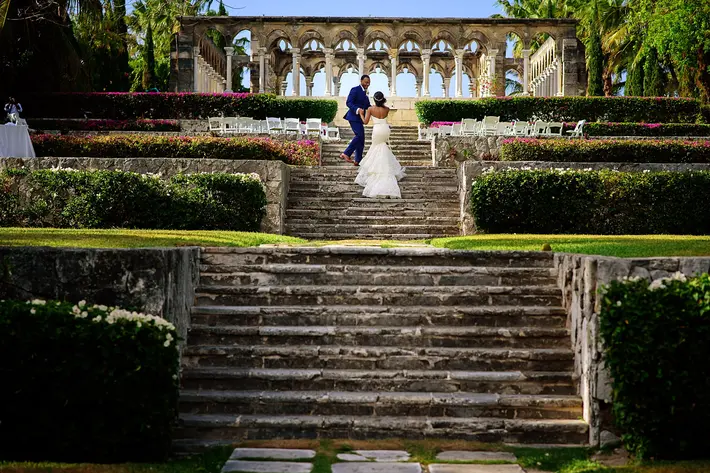 couple-ascend-stairs-to-greek-column-ceremony-bride-with-trumpet-lace-dress-worlds-best-wedding-photos-jide-alakija-new-york