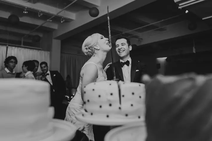 Bride licks frosting from sword used for cake cutting - photo by The Brenizers - New York
