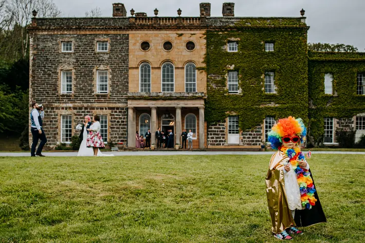 child-in-costume-as-guests-socialize-against-historic-building-m-and-g-wedding-photography