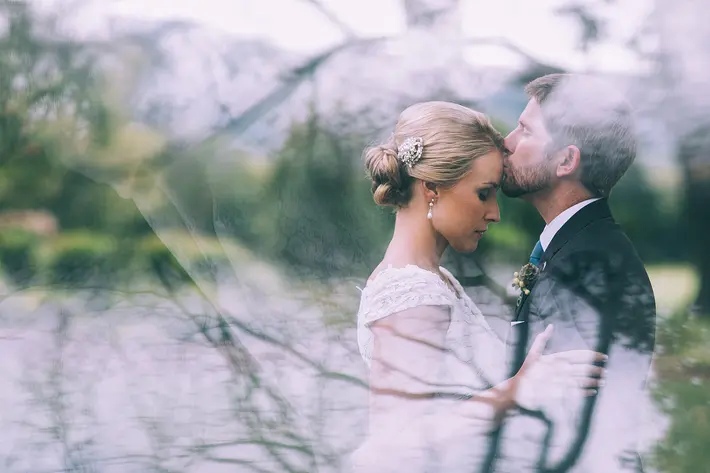 groom-kisses-bride-s-forehead-see-through-reflecting-window-nat-wongsaroj-photography