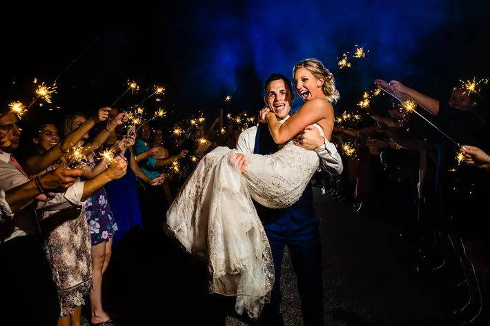 groom-carries-bride-through-path-of-sparklers-smj-photography