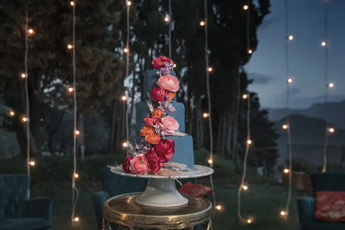 tiered-blue-cake-with-flowers-and-string-lights-photo-by-joanne-dunn-photographers