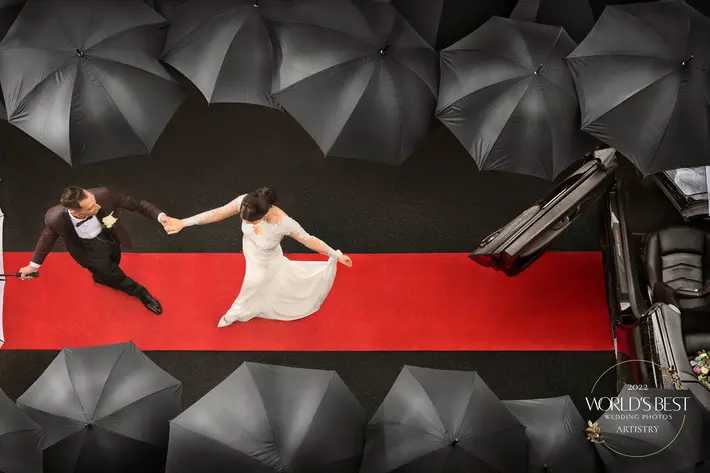 aerial-shot-of-couple-exit-on-to-red-carpet-flanked-by-black-umbrellas-dezine-by-mauro.