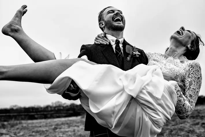 Moment award-winningphoto of groom laughing uproariously with bride held up in his arms - Rich Howman - London