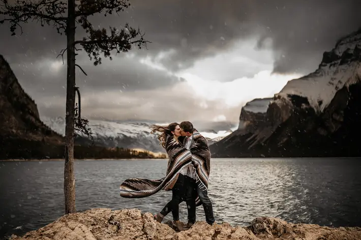 featured-engagement-couple-kiss-at-mountain-lake-edge-with-storm-impending-photo-by-tkshotz-photography