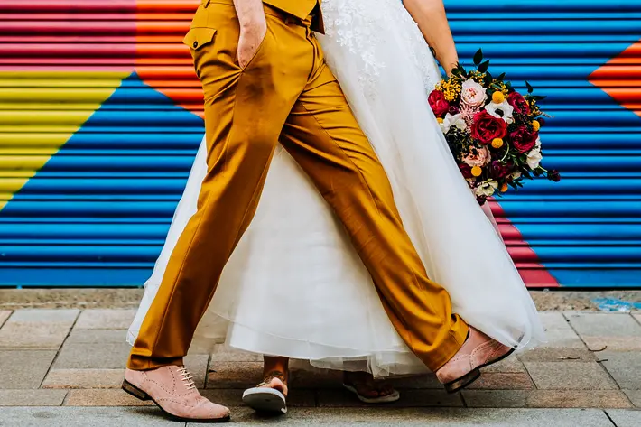 Groom in copper colored suit walking with bride against color block panel M and G Wedding Photography