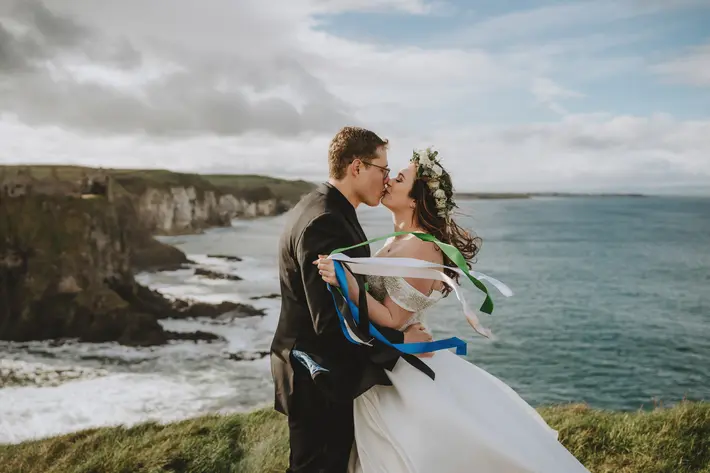 Ireland coast kiss with floral crown and colorful ribbons photo by remain in light photography